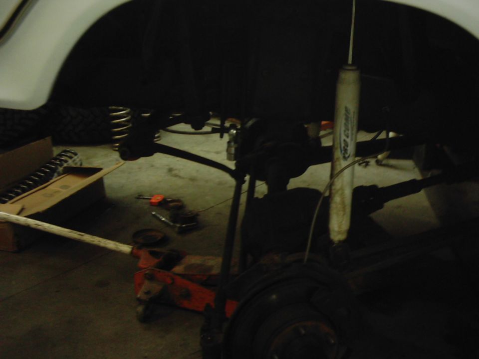 Vehicle suspension components with a jack underneath. A box with springs is to the left