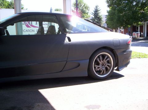 1993 Ford Probe - The side profile of a matte black 1993 Ford Probe is visible, aftermarket wheels and a dark body kit.