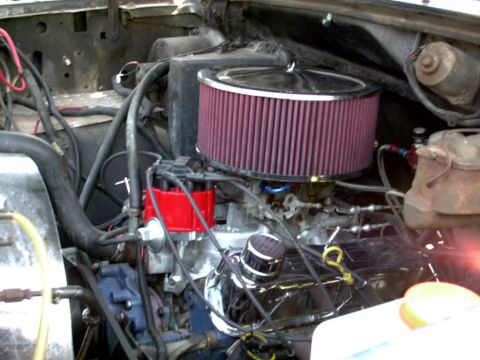 1986 Ford Bronco - Engine bay view down onto a carbureted V8 wearing a large chrome-topped round air cleaner with a red pleated washable filter element. Below…
