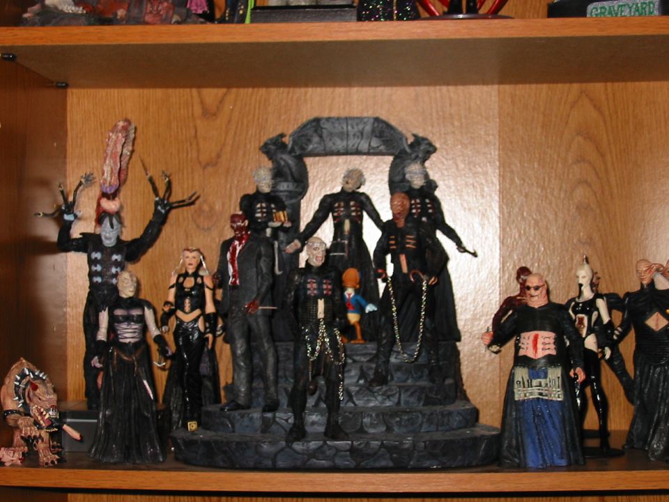 Collection of horror movie action figures, including Pinhead and other Cenobites, displayed on wooden shelves