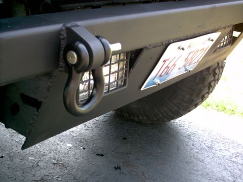 1986 Ford Bronco - Close-up of a flat gray/olive steel front bumper on a truck or SUV, fitted with a black D-ring shackle and mount, a mesh grille panel, and…