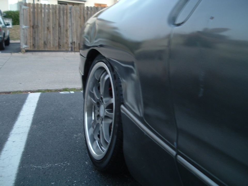 Front wheel of dark gray coupe with silver alloy wheel and red brake caliper in parking lot