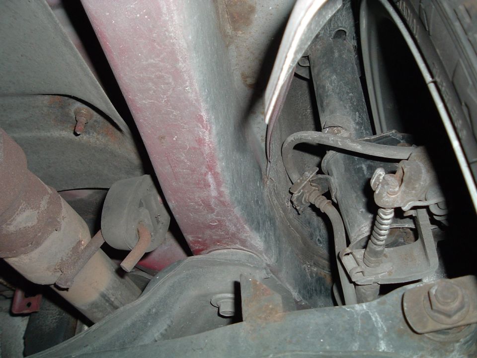 Underbody view of rear suspension with strut, brake lines, exhaust hanger, and tire visible