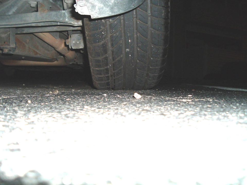 Ground-level view of a car tire and undercarriage components on asphalt