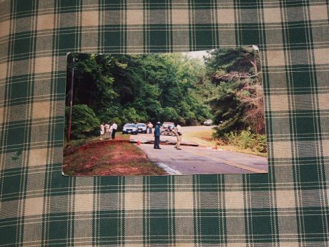 1966 Ford Ranchero - A group of individuals are gathered near several vehicles on a road, with a wooded area in the background.