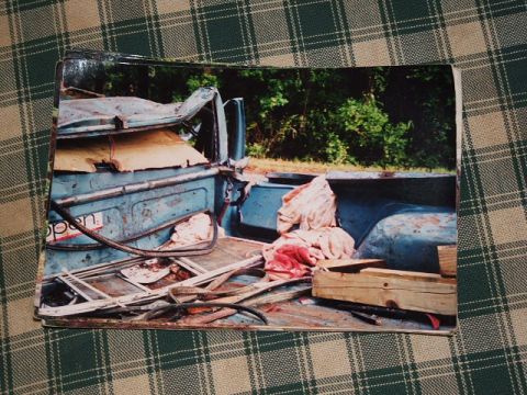 1966 Ford Ranchero - The rear of a damaged blue pickup truck bed is filled with debris, including fabric and wood.