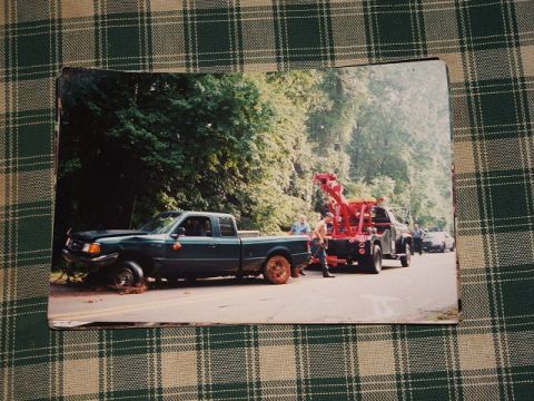 1966 Ford Ranchero - A tow truck is assisting a pickup truck that appears to have a damaged front tire on a tree-lined road.