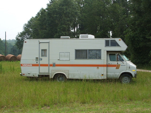 White Midas RV with orange stripes parked in grassy field