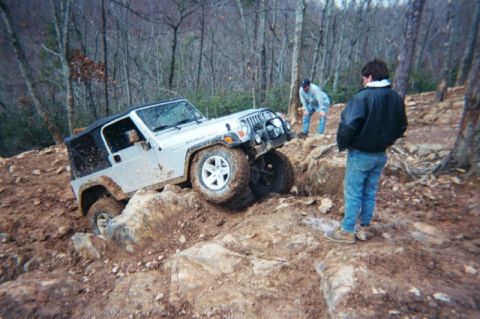 1985 Ford Bronco - A Jeep Wrangler Rubicon navigates a challenging off-road course with two onlookers.