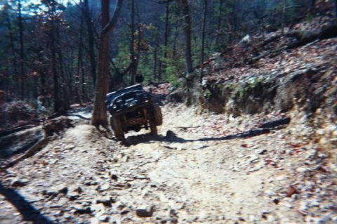 1985 Ford Bronco - An off-road vehicle navigates a challenging dirt path through a wooded area.