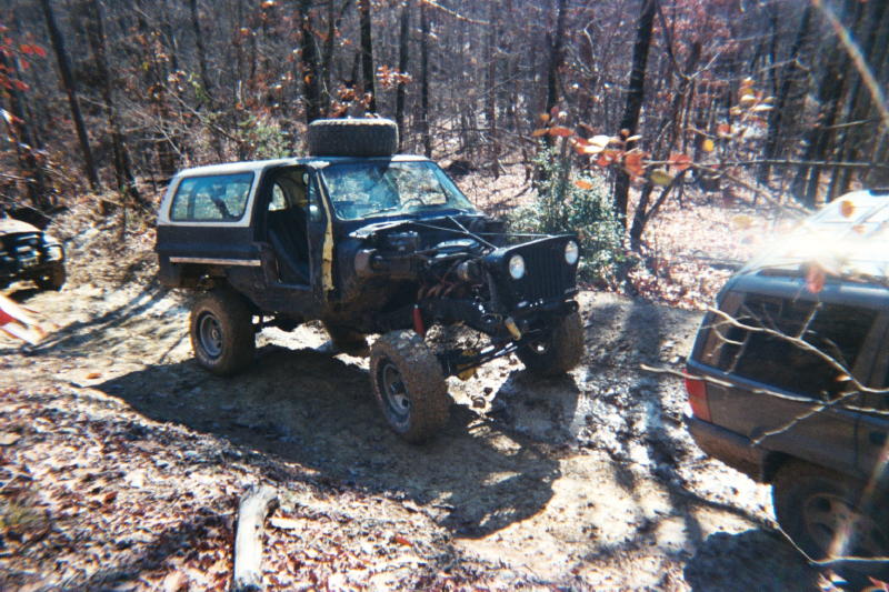 Modified SUV with hood removed, spare tire on roof, driving off-road with another SUV nearby