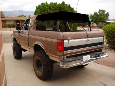 1989 Ford Bronco - This 1989 Ford Bronco features a black soft top, lifted suspension, and large off-road tires, suggesting it is modified for off-road use.
