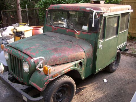 1973 Jeep CJ5 - This weathered panel van, possibly a modified Jeep, sits in a yard with visible rust and a custom rear cargo area.