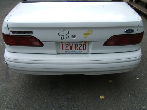 1998 Ford Taurus - The rear of a white 1998 Ford Taurus sedan is shown, its distinctive taillights and a Massachusetts license plate.