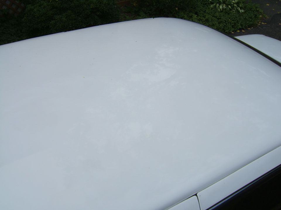 White car roof with some discoloration, green foliage in background. SUPERMOTORS watermark visible
