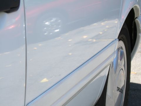 1998 Ford Taurus - A white 1998 Ford Taurus is seen from the side, with the door trim and wheel clearly visible.