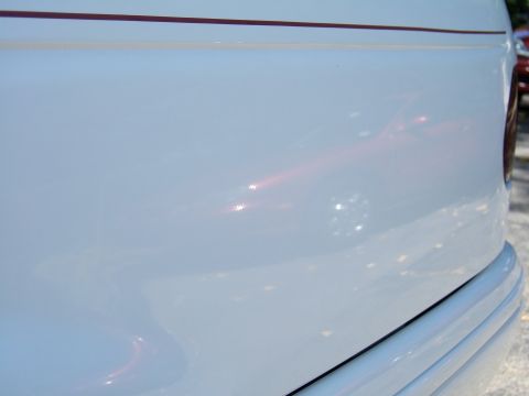 1998 Ford Taurus - Close-up of a white car's rear quarter panel, showing a subtle stripe and trim detail. The vehicle's year is not discernible from this view.