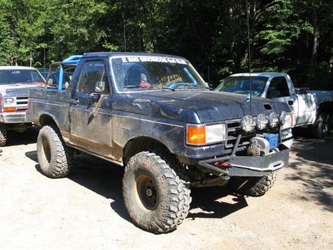1989 Dodge Power Ram - A modified dark blue pickup truck with off-road lights and a winch is parked next to other vehicles.