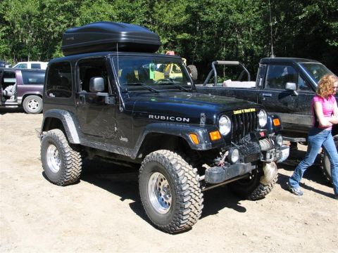 1989 Dodge Power Ram - A modified black Jeep Wrangler Rubicon is parked outdoors with a cargo box on its roof, alongside other vehicles.