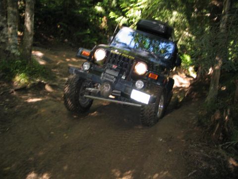 1989 Dodge Power Ram - A Jeep Wrangler TJ navigates a steep, wooded trail with its headlights on.