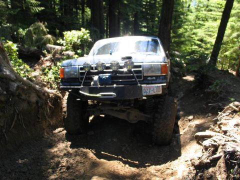 1989 Dodge Power Ram - A modified Ford F-series truck navigates a challenging off-road trail in a wooded area.