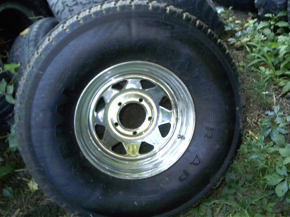 spare tire with a chrome rim, stacked with other tires outdoors