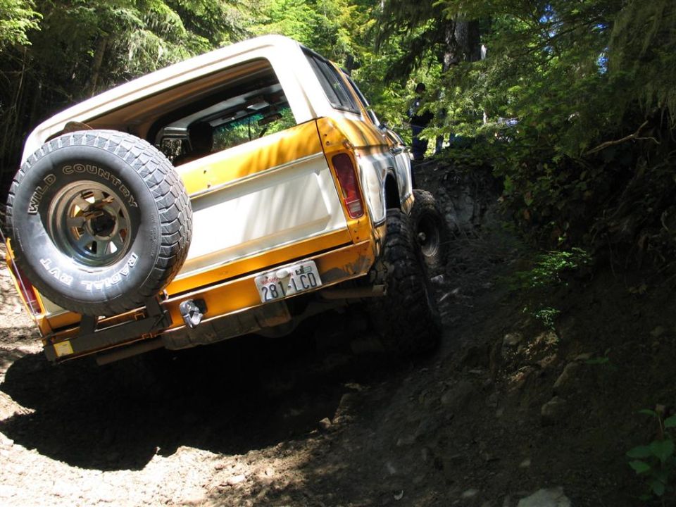 Yellow and white off-road vehicle with spare tire on rear, driving on a dirt trail