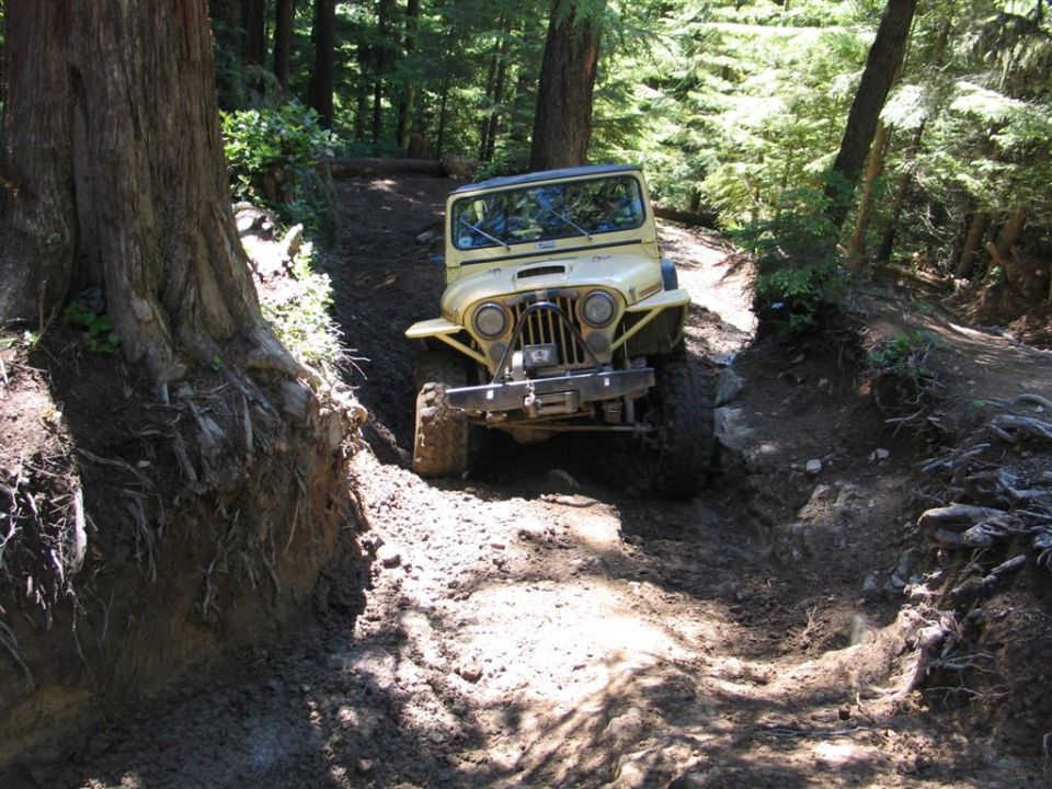 Yellow Jeep CJ-7 on a muddy forest trail, front view