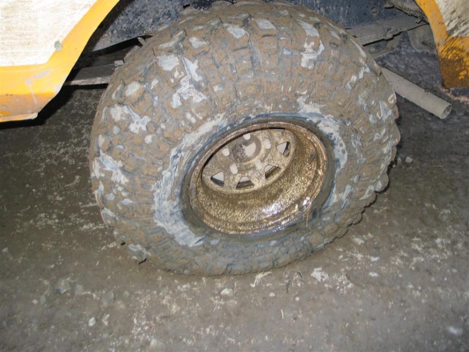Flat mud-caked oversize mud-terrain tire on steel wheel lying on shop floor