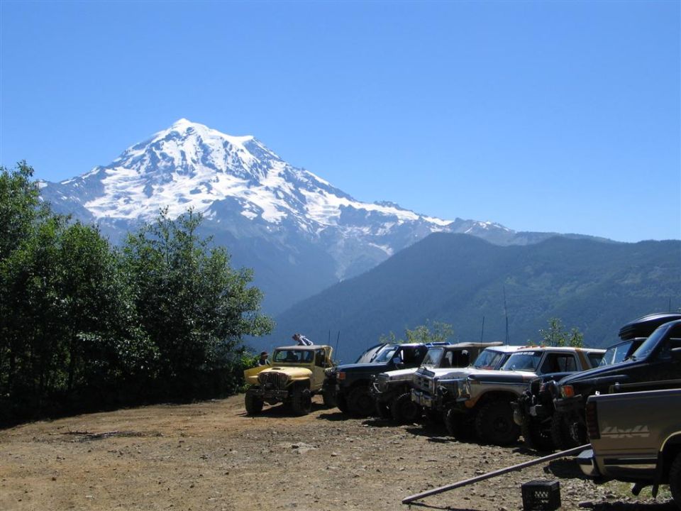 Yellow jeep and other off-road vehicles parked with a snowy mountain in the background