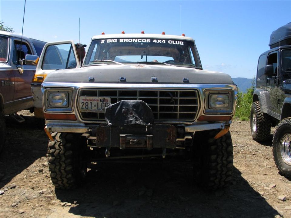 Front view of a 1979 Ford F-Series truck with a winch and off-road tires. Another truck and a Jeep are parked nearby
