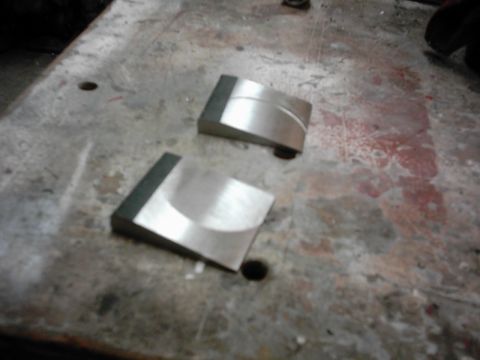 1978 Ford Bronco - Two machined metal components rest on a stained and worn workbench surface.