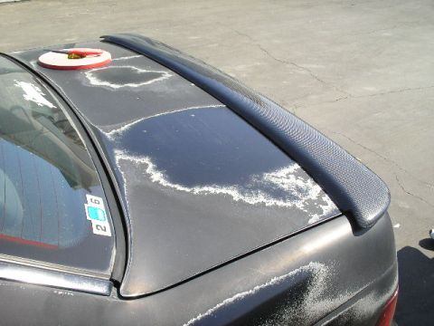 1991 Ford Taurus - The rear of a car shows significant paint damage and a carbon fiber spoiler.