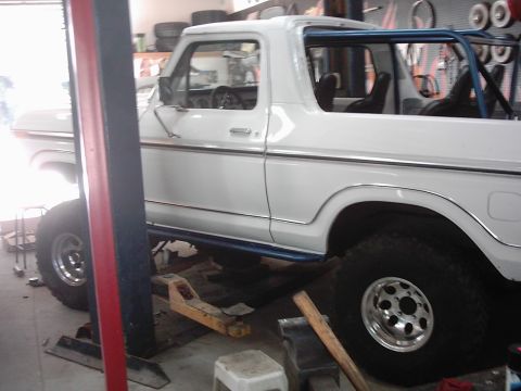 1978 Ford Bronco - A white 1978 Ford Bronco is shown on a hydraulic lift in a garage, with a blue roll cage visible.