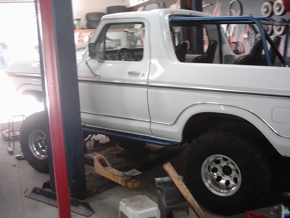 White 1978 Ford Bronco with blue roll cage, lifted on a service lift
