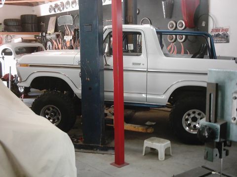 1978 Ford Bronco - A white 1978 Ford Bronco is parked on a lift inside a garage, showing its side profile and a blue roll cage.