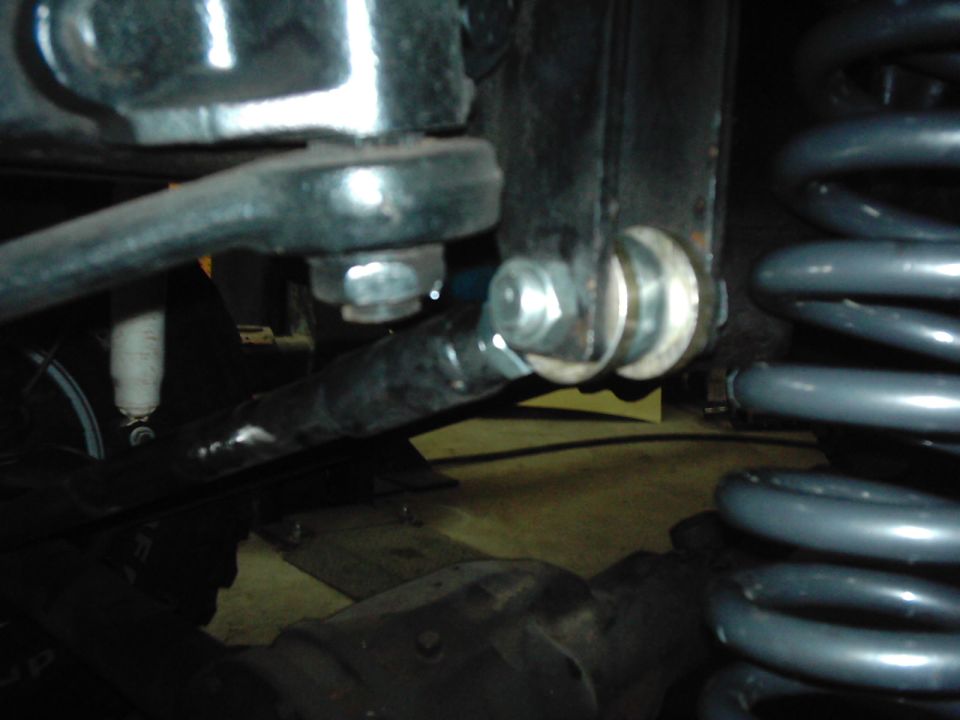 Close-up of a black metal linkage connected to a bracket with bolts and washers, next to a gray coil spring