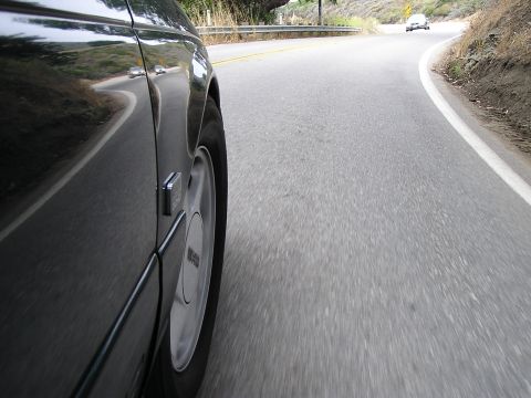 1993 Ford Taurus - A car travels down a two-lane road with a guardrail and dry brush on the side.