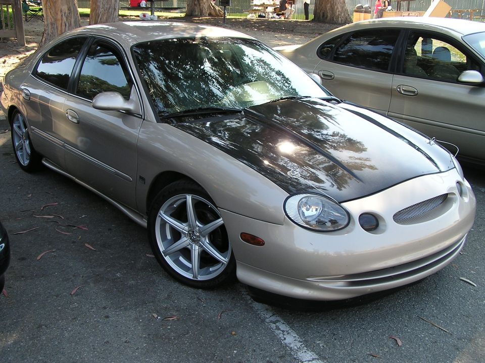 Tan Ford Taurus with a black hood, parked next to another car