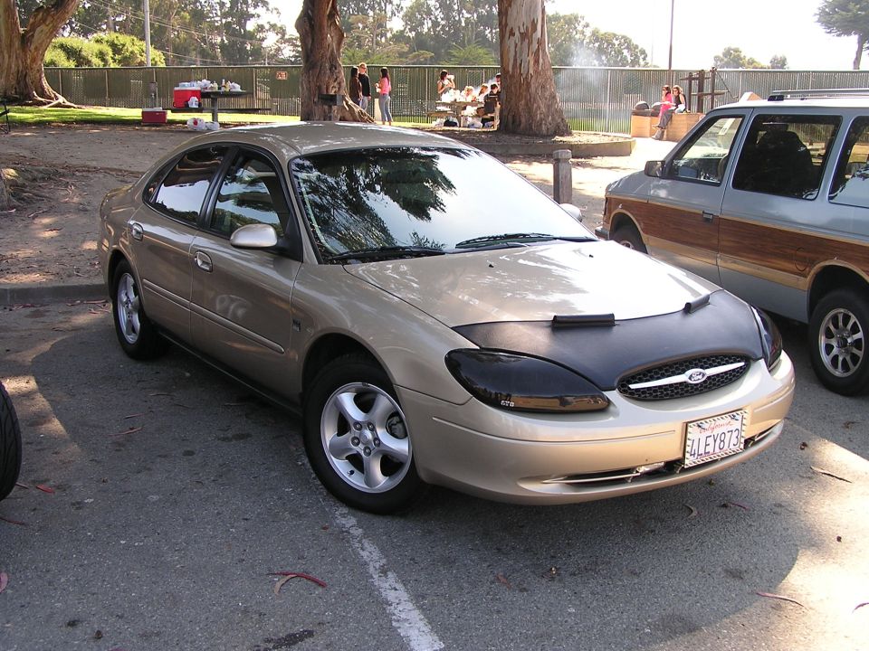 Gold sedan with black car bra and tinted headlights parked on asphalt