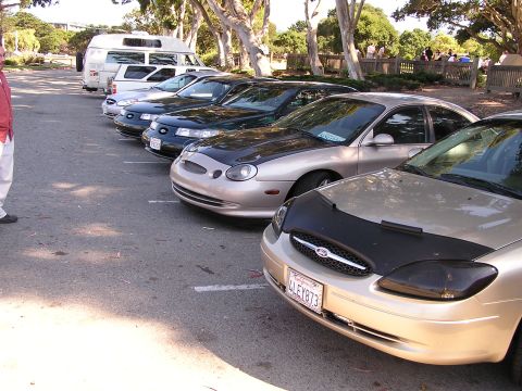 1993 Ford Taurus - A line of cars, including a gold Ford Taurus, are parked in a lot on a sunny day.