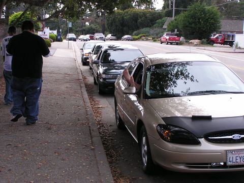 1993 Ford Taurus - A tan sedan is parked on the street, with a person's legs visible hanging out the driver's side window.