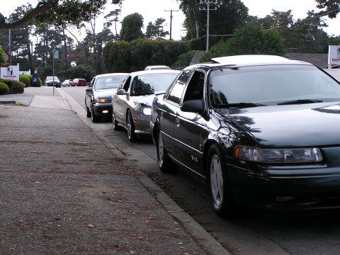 1993 Ford Taurus - Several cars are parked along a curb on a street, with the front of a 1993 Ford Taurus in the foreground.