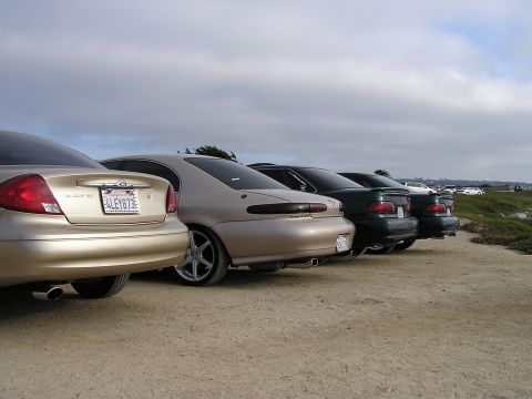 1993 Ford Taurus - A line of sedans are parked on a dirt lot with a cloudy sky overhead.