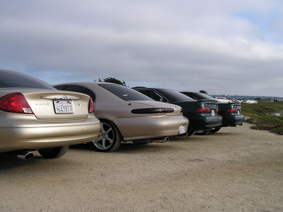 Four sedans parked in a row, facing away from the camera. The closest car is gold, followed by a tan one, then two dark green cars