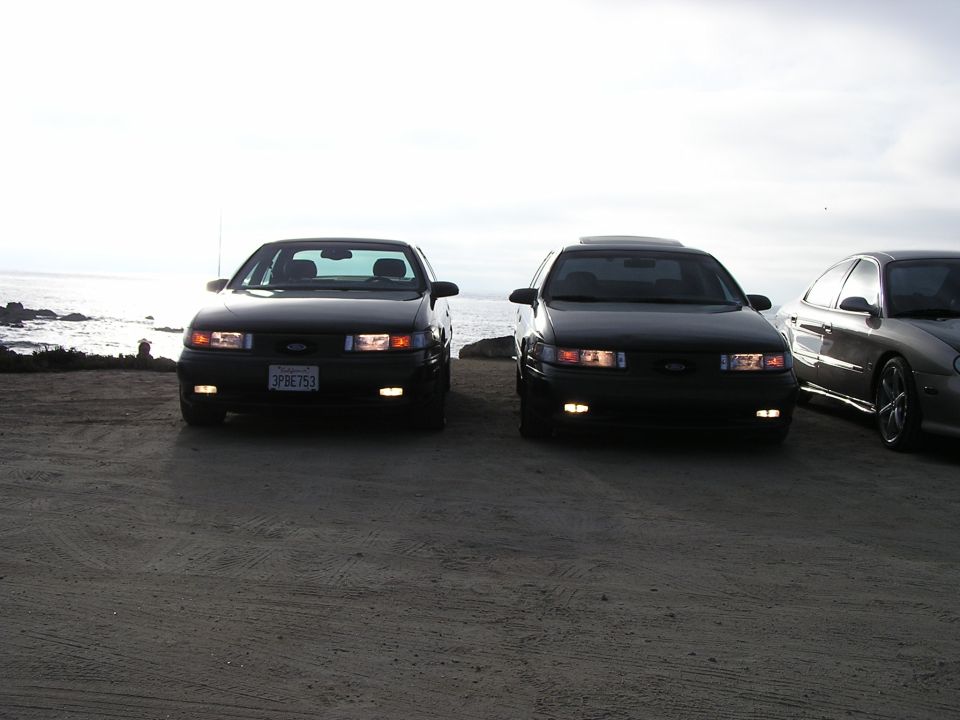 two black Ford Taurus sedans parked by the ocean