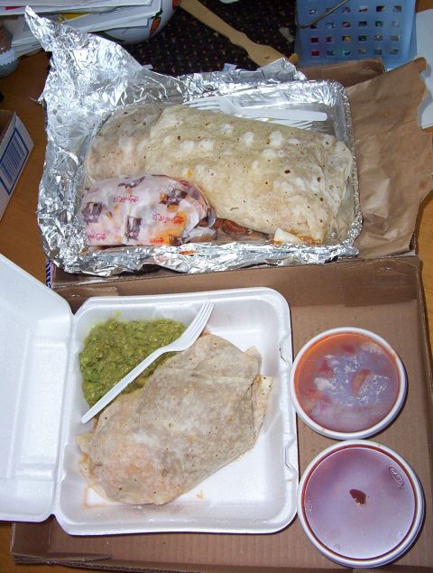 1995 Ford Bronco - Two large burritos, one wrapped in foil and another in a styrofoam container with guacamole, are ready to be eaten.