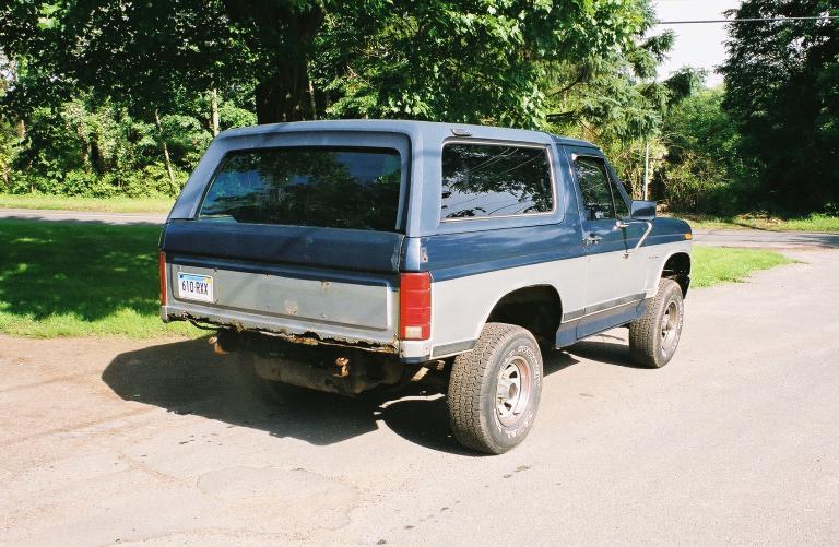 Two-tone blue and gray Ford Bronco, rear view, showing a dented rear bumper and a license plate reading '610 RKX'