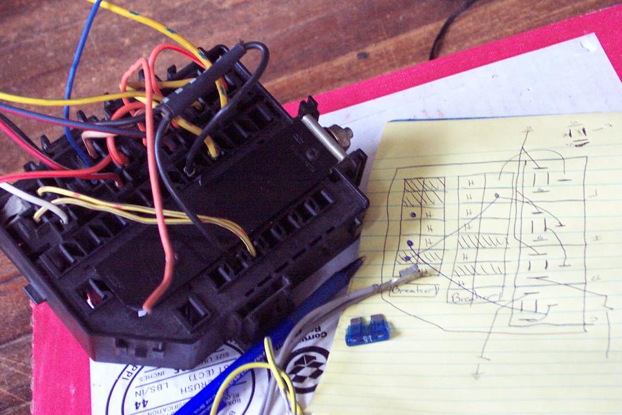 Fuse box with colored wires on a yellow notepad showing a hand-drawn wiring diagram, with two blue blade fuses nearby