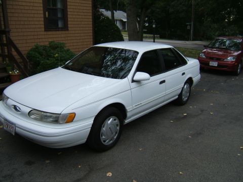 1998 Ford Taurus - A white 1998 Ford Taurus is parked in front of a house, with another vehicle visible in the background.